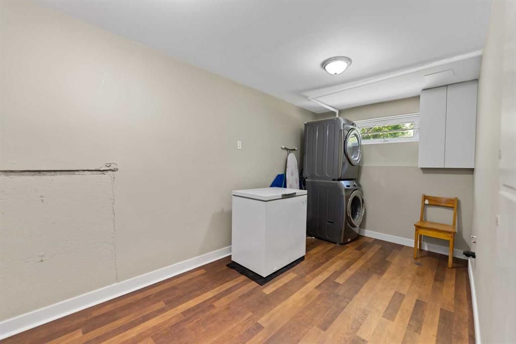 Laundry room with washer and dryer, white cabinet, wooden chair, and wood floor