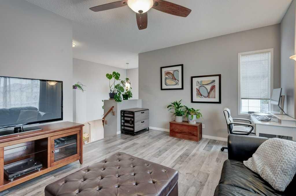 Bright living room with gray walls, TV, sofa, plants, and a ceiling fan