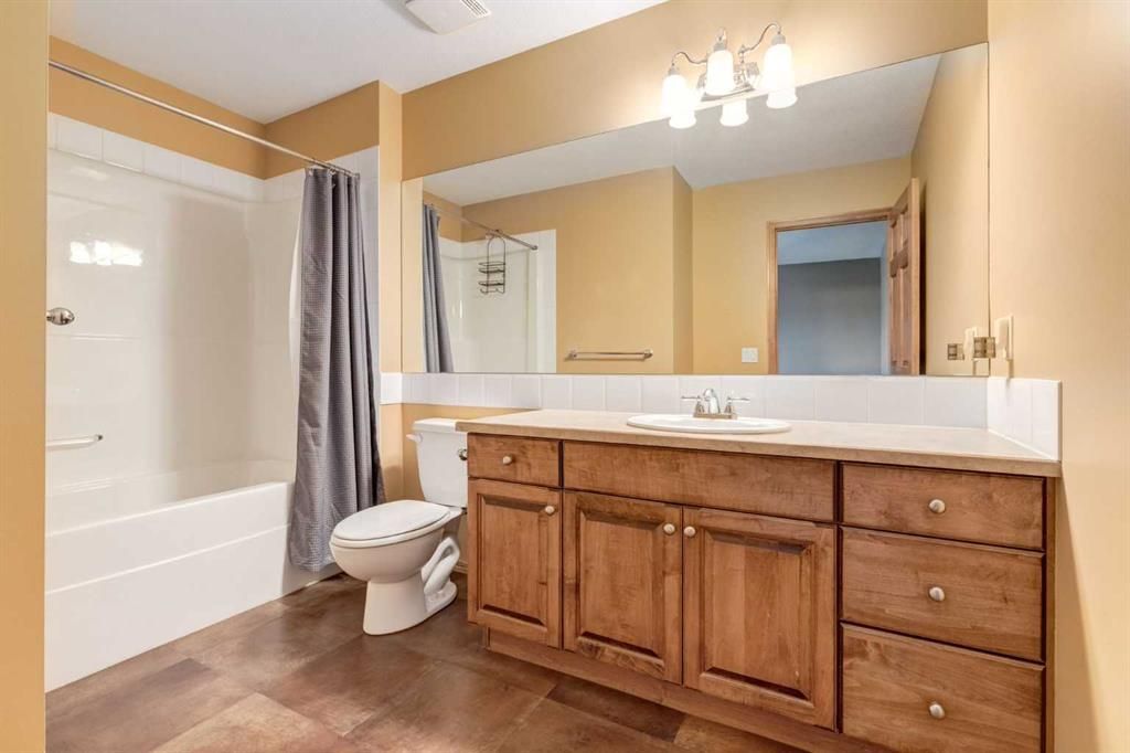 Bathroom with wood vanity, large mirror, toilet, tub with gray curtain, and beige walls