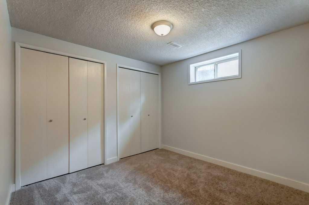 Empty beige bedroom with carpet, closet doors, and a small high window.