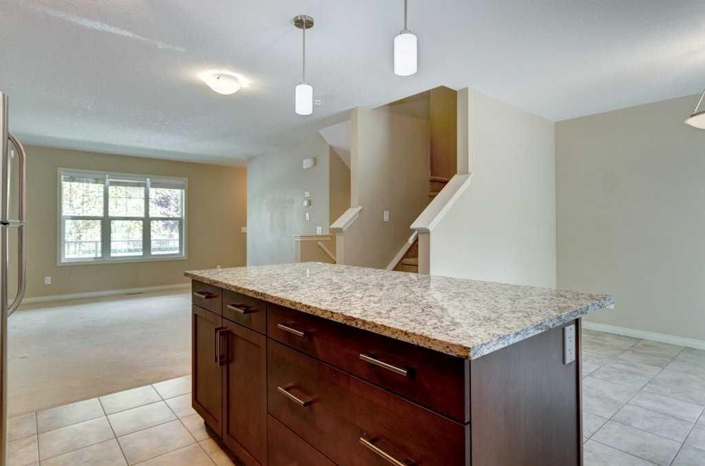 Empty kitchen with granite island, pendant lights, and a windowed living area.