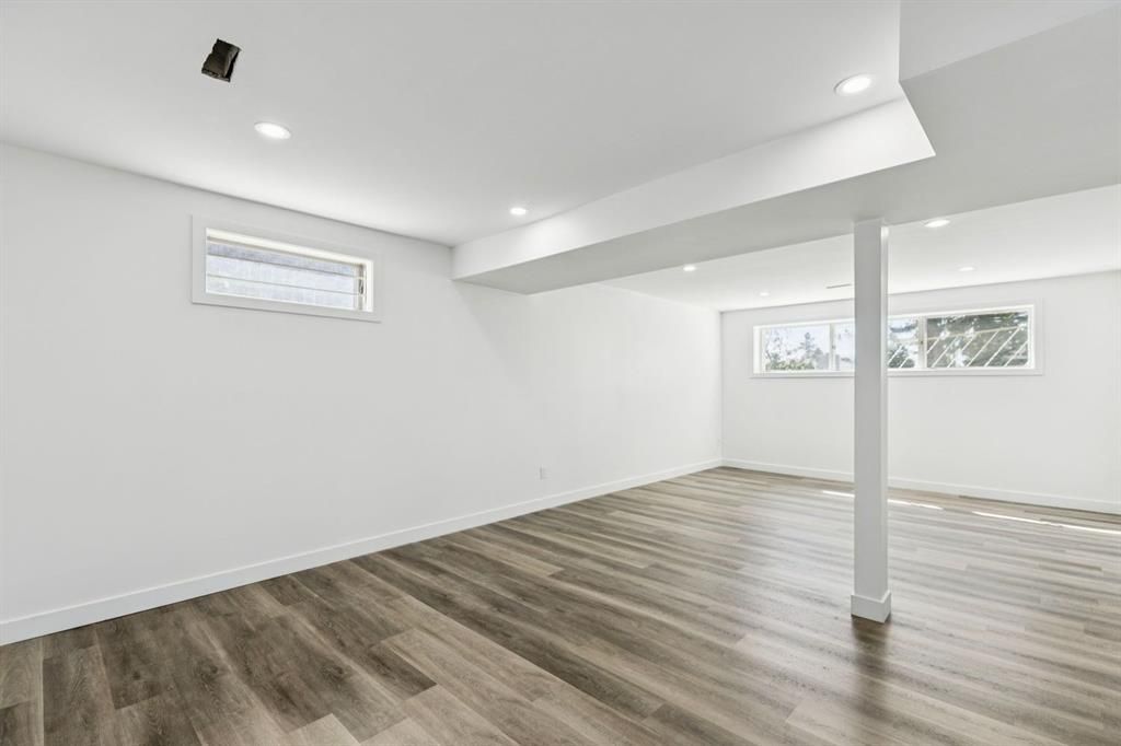 Empty white room with wood-look flooring, recessed lights, and small high windows
