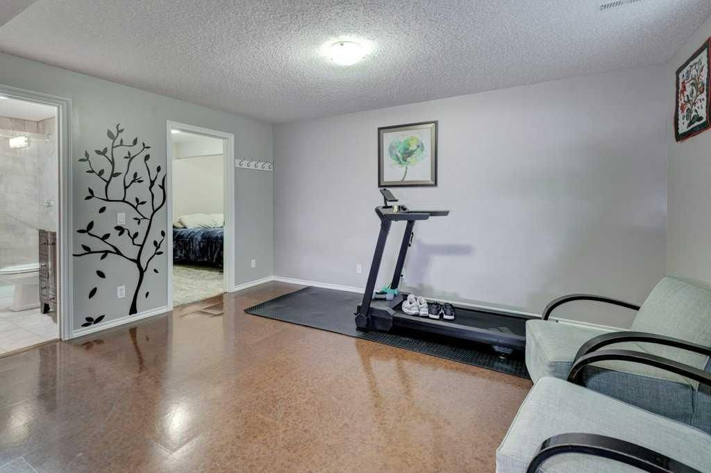 Bright living room with treadmill, white walls, wood floor, wall art, and chairs by the window.
