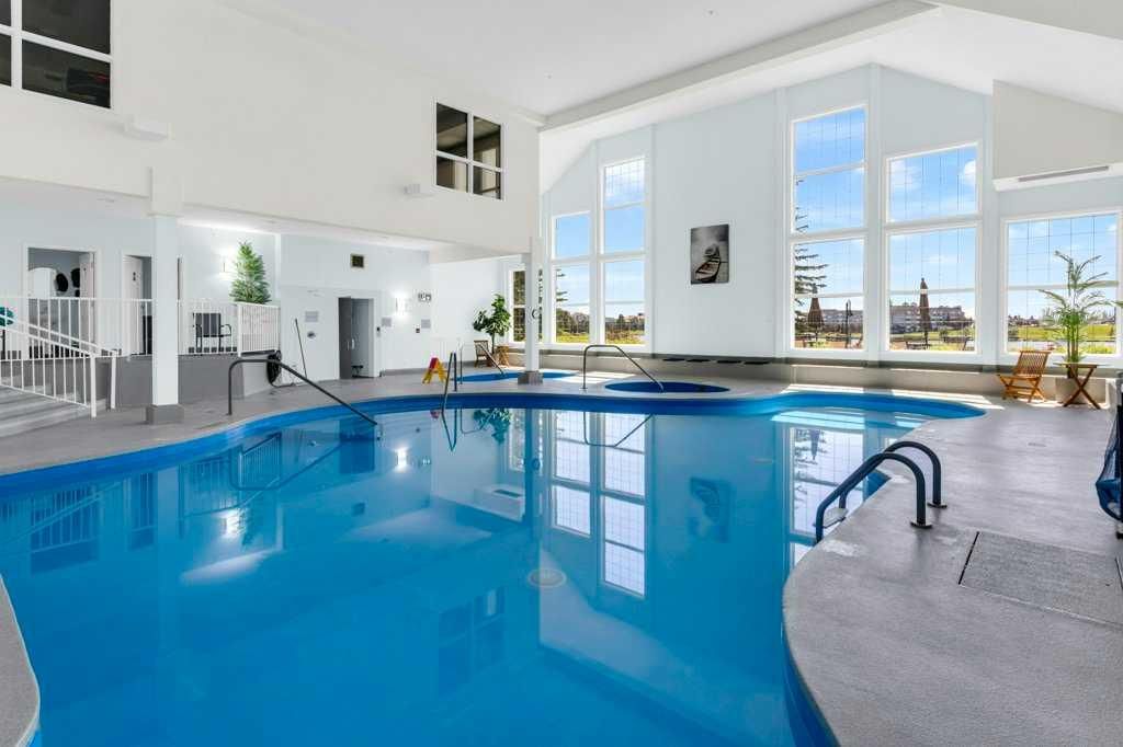 Indoor swimming pool with bright windows, blue water, and lounge chairs overlooking a snowy landscape