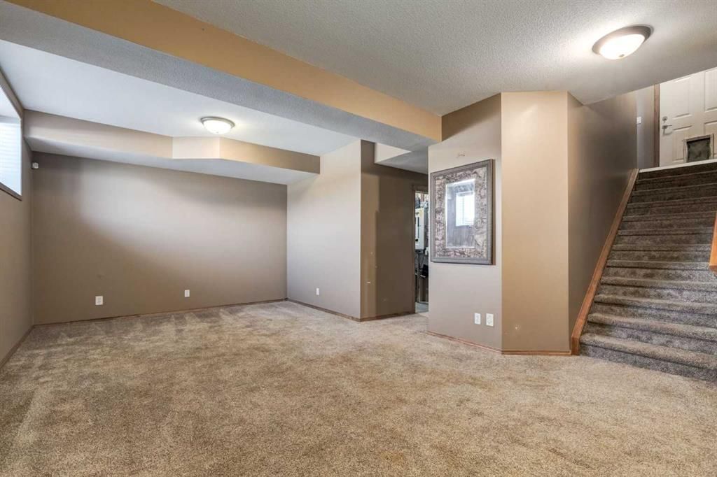 Empty carpeted basement room with beige walls, recessed lights, and stairs on the right