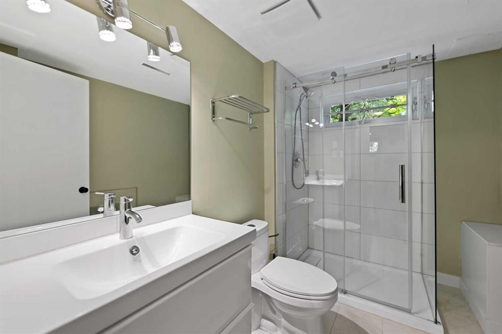 Modern bathroom with glass shower, white sink, toilet, and pale green walls