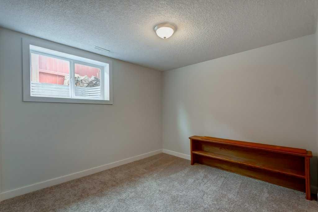 Empty beige room with carpet, a small window, ceiling light, and a wooden bench against the wall