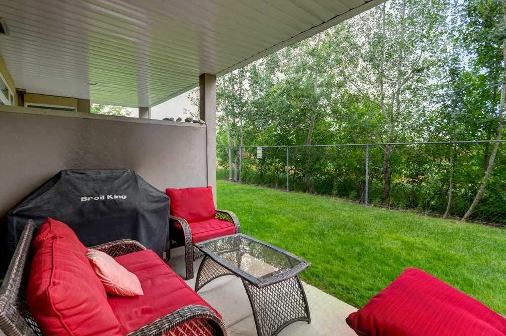 Covered patio overlooking green lawn and trees, with red cushioned chairs and a glass table.