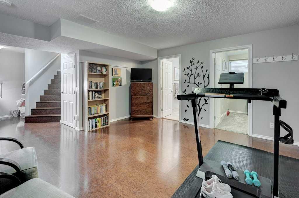 Spacious basement with wood floor, staircase, bookshelf, dresser, and treadmill near white walls.