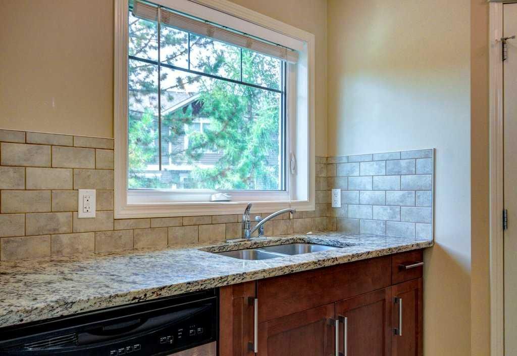 Kitchen countertop and sink under a window with granite counters, wood cabinets, and light tile backsplash