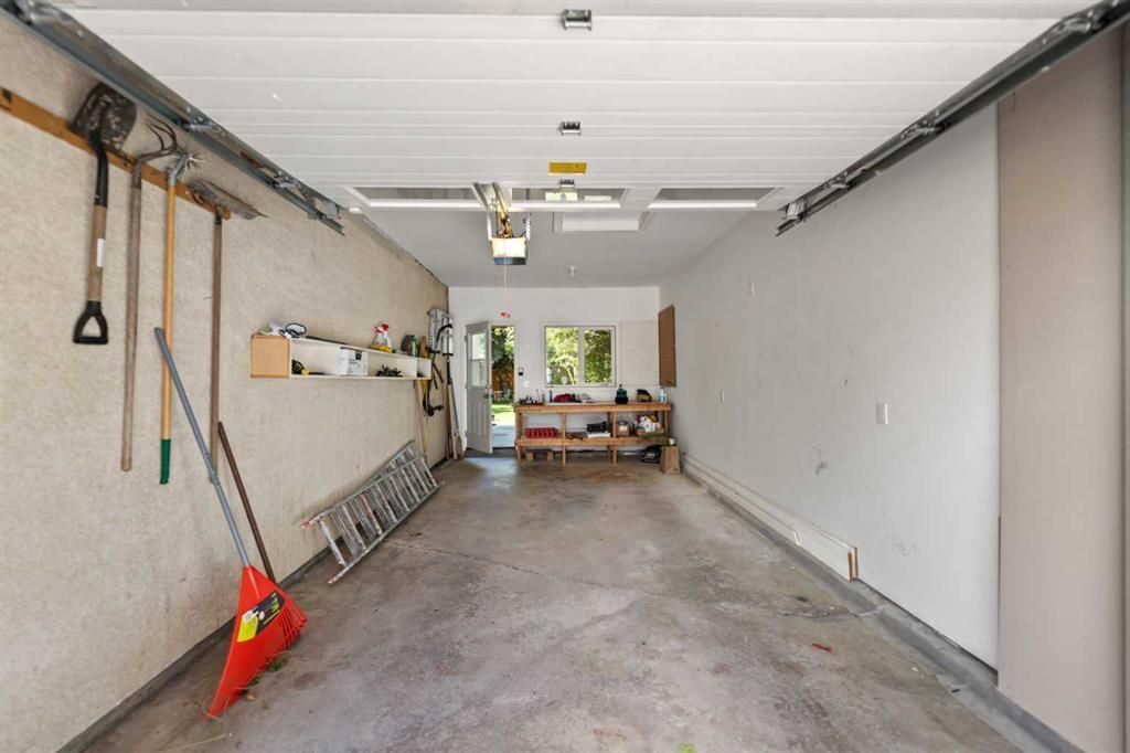 Garage interior with gray concrete floor, white walls, tools on the left, and a workbench at the back.