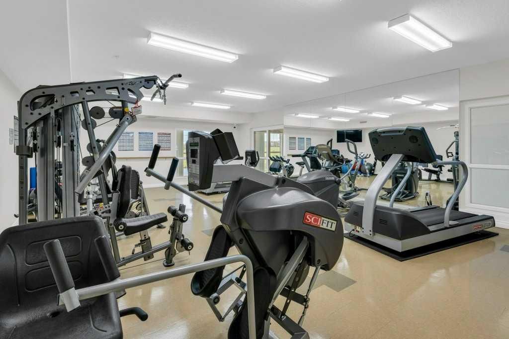 Bright gym with treadmills, weight machines, and mirrored walls under fluorescent lights