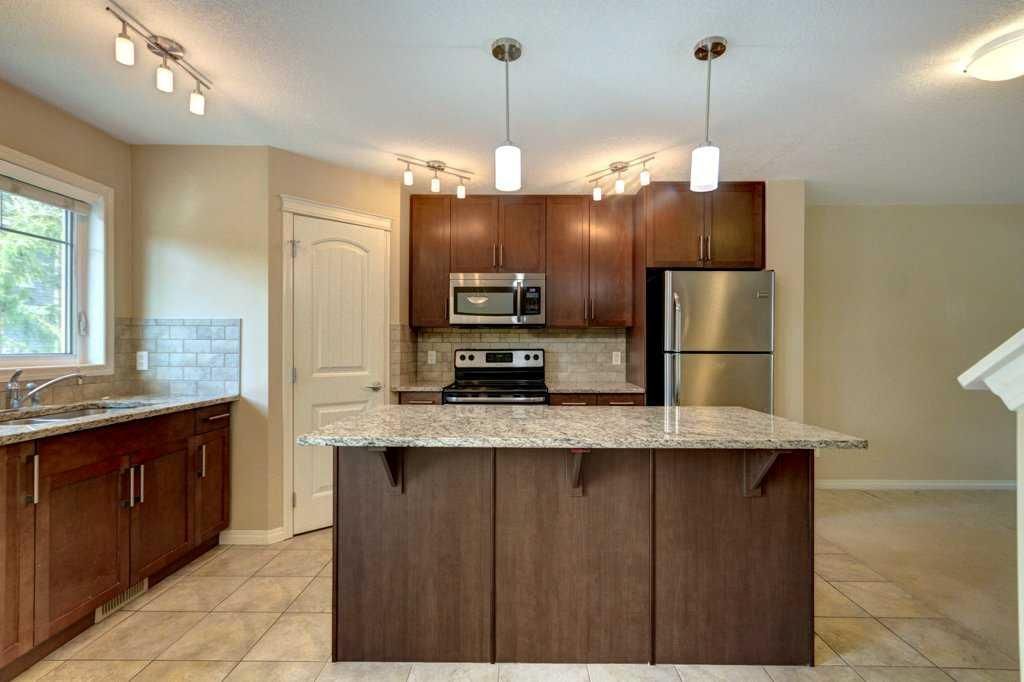 Modern kitchen with dark wood cabinets, granite island, stainless appliances, and tiled floor
