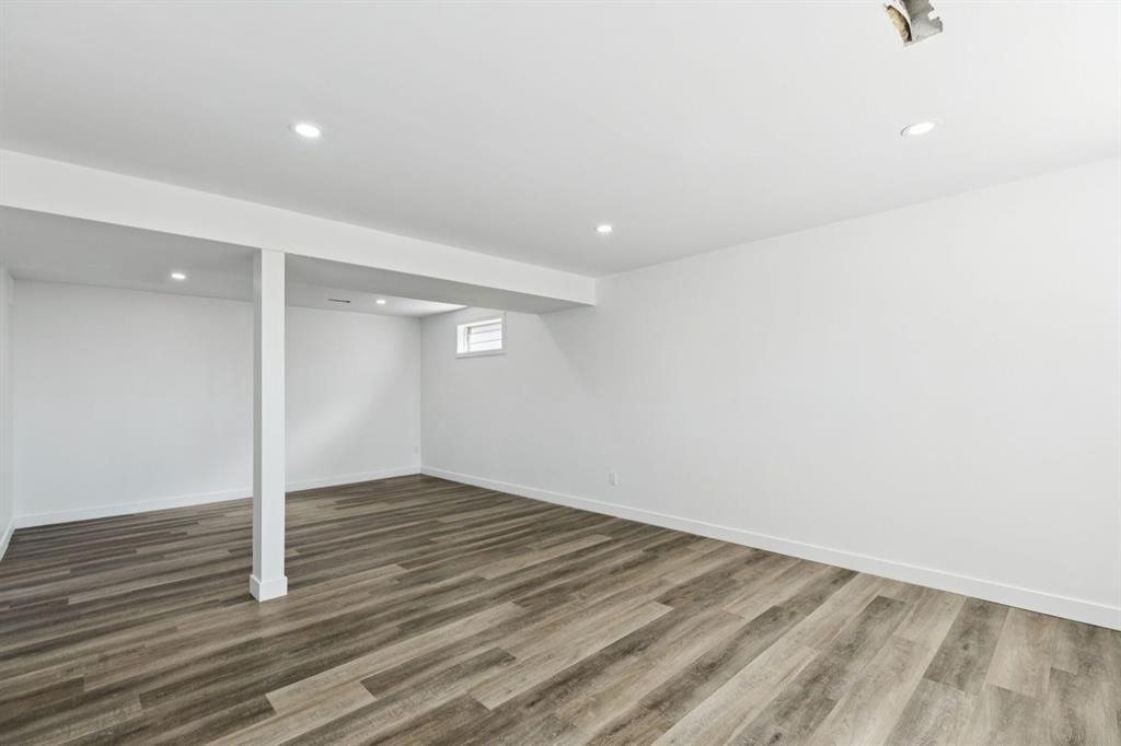 Empty white basement room with gray wood floors, recessed lights, and a support column