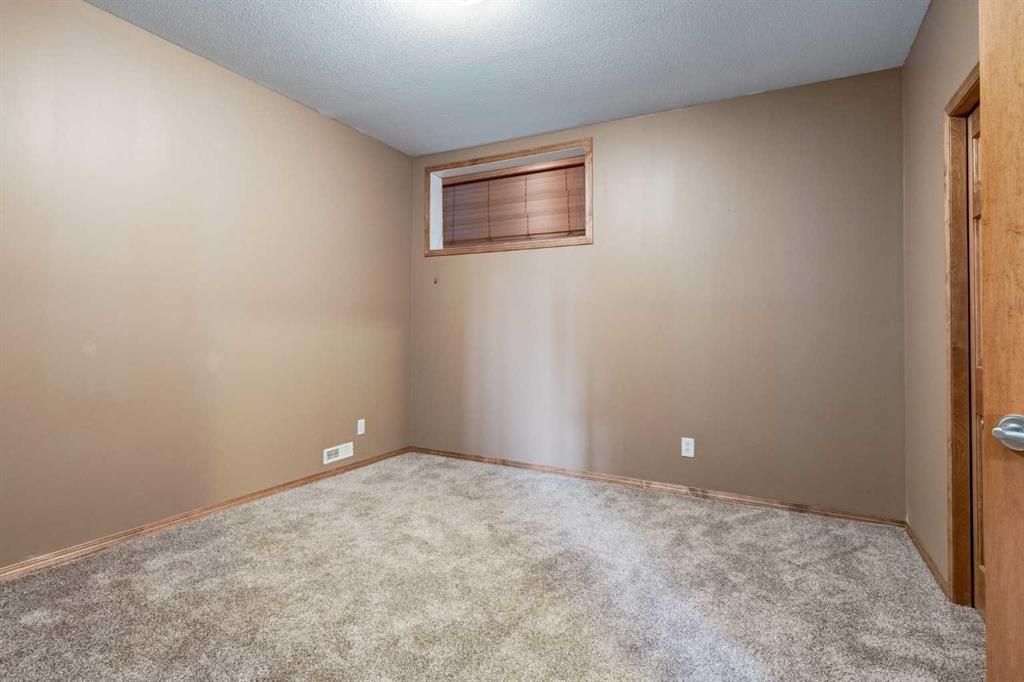 Empty beige bedroom with carpet, small window, and a wooden door