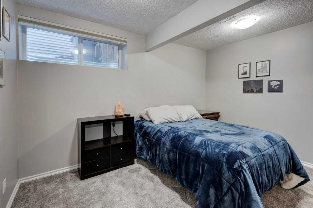 Small bedroom with a bed, black nightstand, gray carpet, and two small windows.