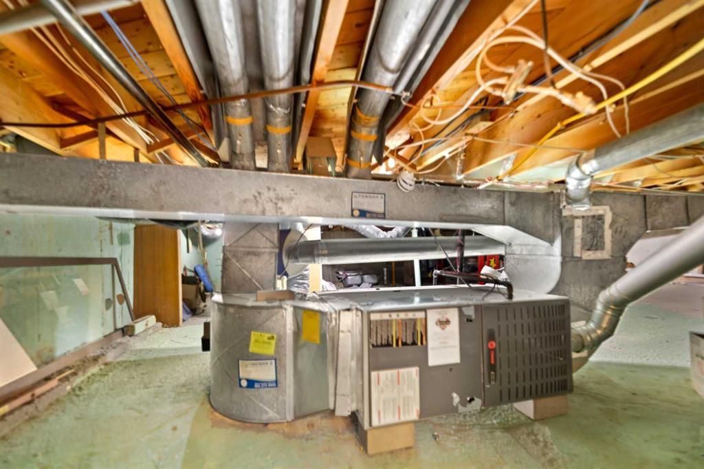 Large HVAC furnace and ductwork in a basement utility room with exposed ceiling beams.
