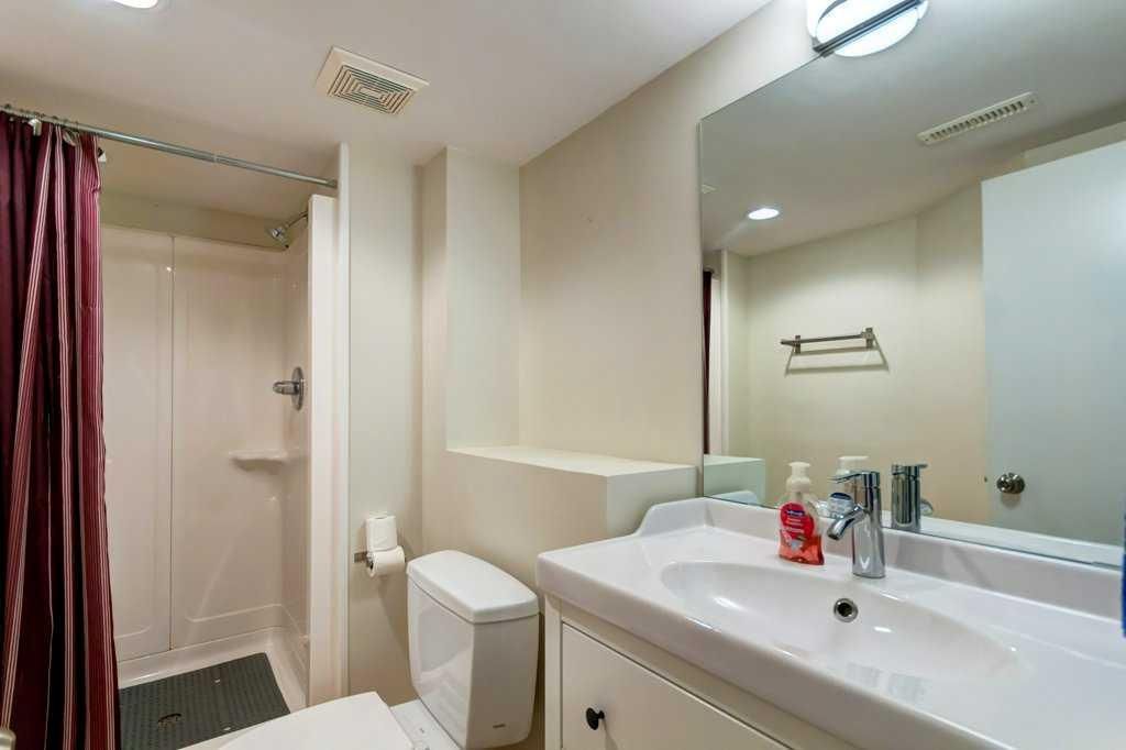 Bathroom with white vanity sink, mirror, toilet, and shower stall in a light-colored interior