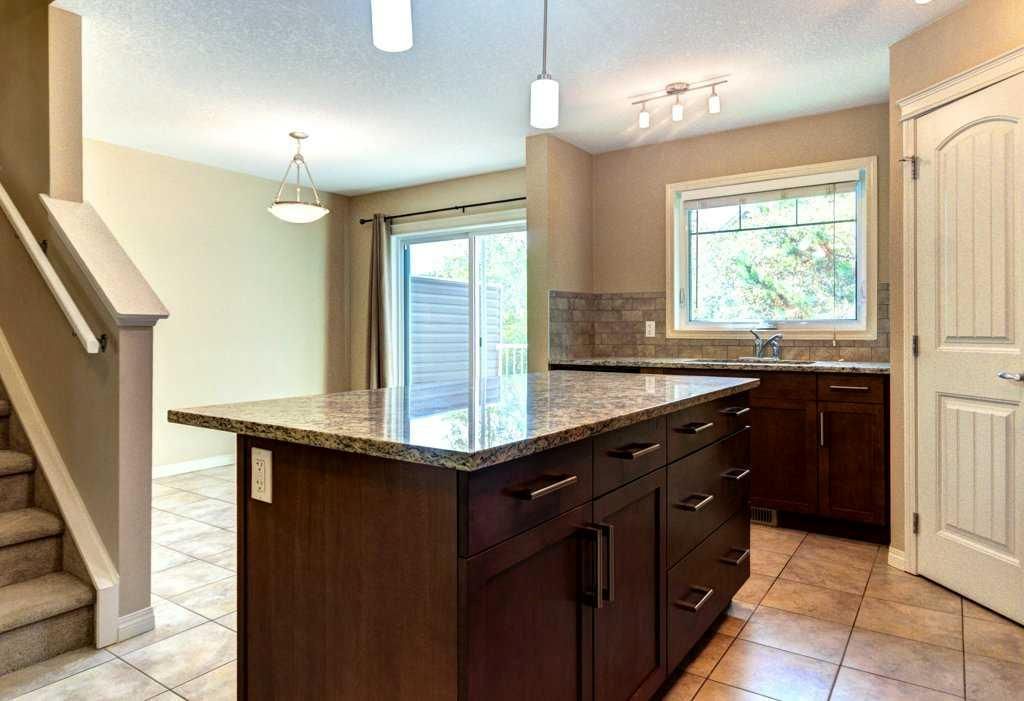 Bright kitchen with dark island, tan cabinets, tile floor, and sliding glass door to outside