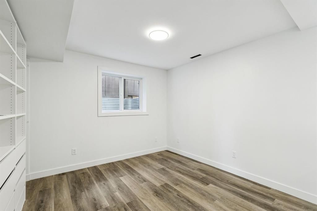 Empty white bedroom with wood flooring, a small window, and built-in shelving.