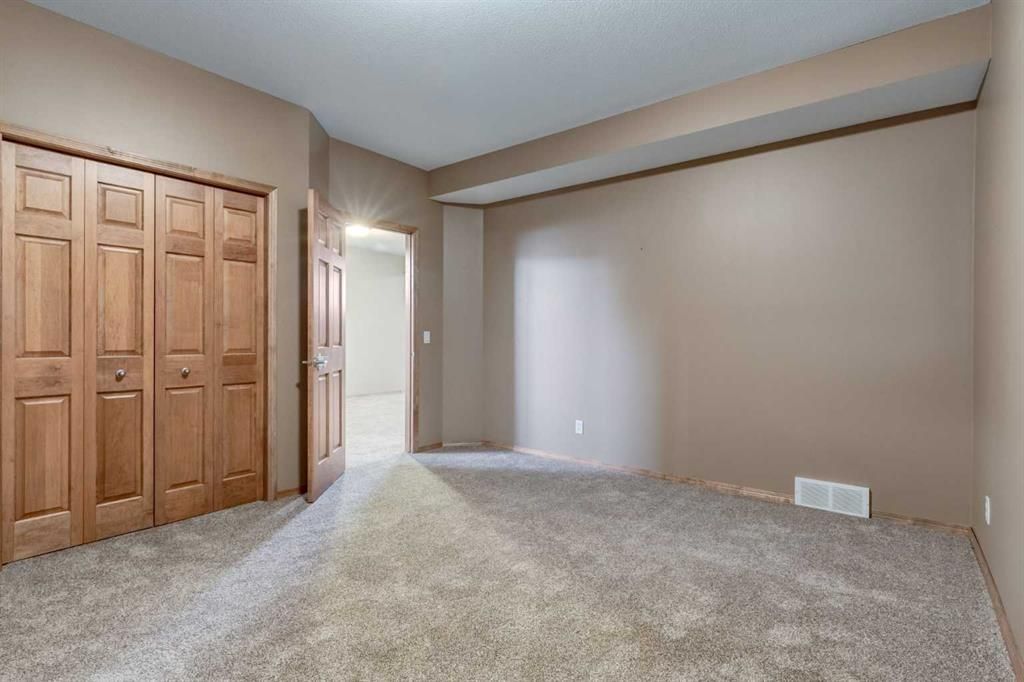 Empty beige bedroom with carpet, closet doors, and a doorway to the hall