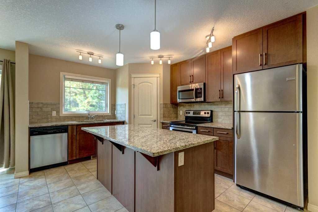 Modern kitchen with granite island, wood cabinets, stainless steel appliances, and tiled floor