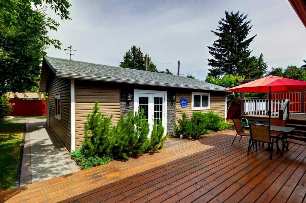 Small backyard cabin with deck, patio table, red umbrella, and surrounding greenery