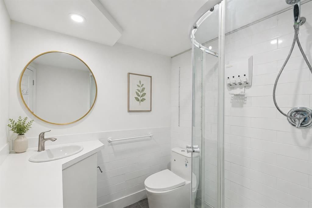 Bright white bathroom with round mirror, sink, toilet, and glass shower enclosure