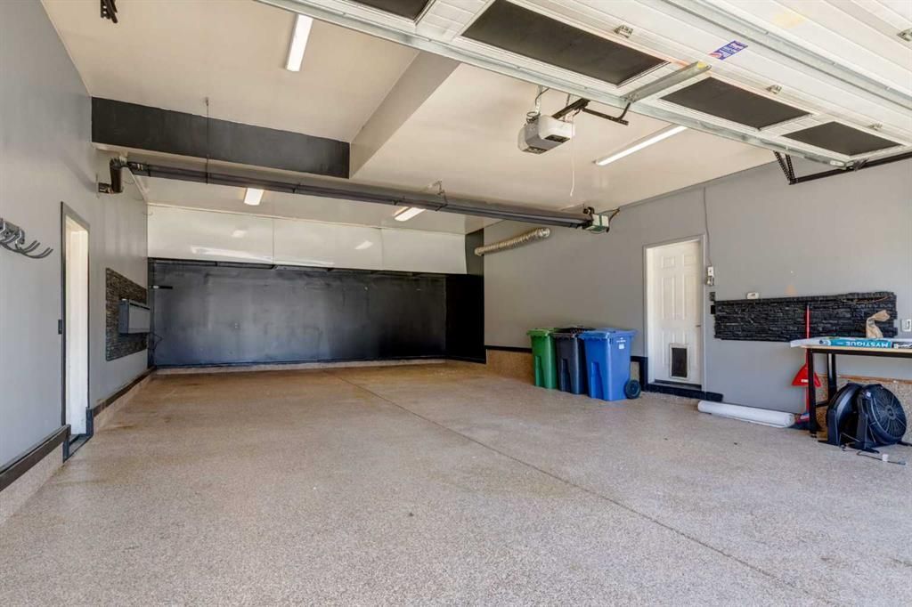 Empty indoor garage with speckled floor, black back wall, overhead lights, and bins along the right side