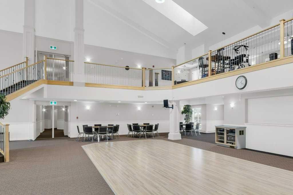 Bright, empty banquet hall with white walls, balcony railing, tables, chairs, and a wood dance floor