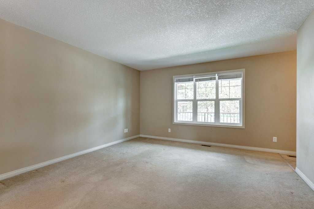Empty beige living room with carpet, white trim, and a window letting in daylight