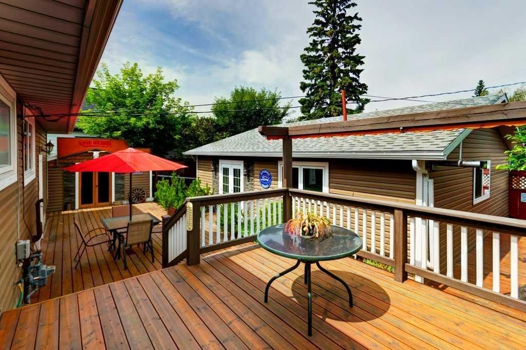 Wooden deck patio with red umbrella, glass table, and railing overlooking a courtyard and trees