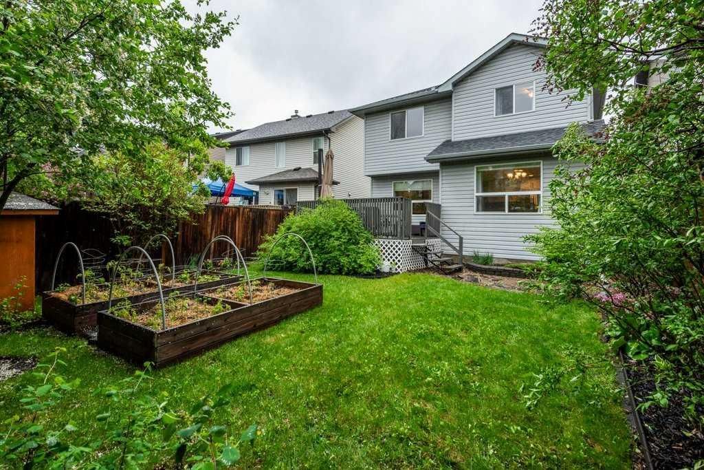 Backyard garden with green lawn, raised planter bed, and white house in the background