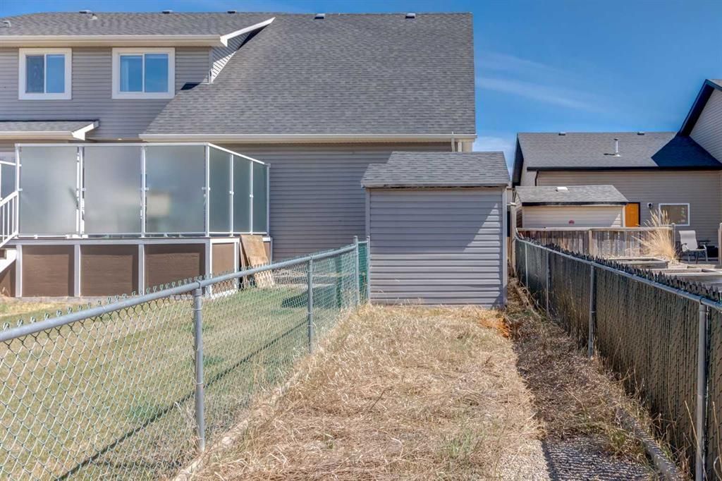 Backyard with narrow grass path between chain-link fences and neighboring houses.