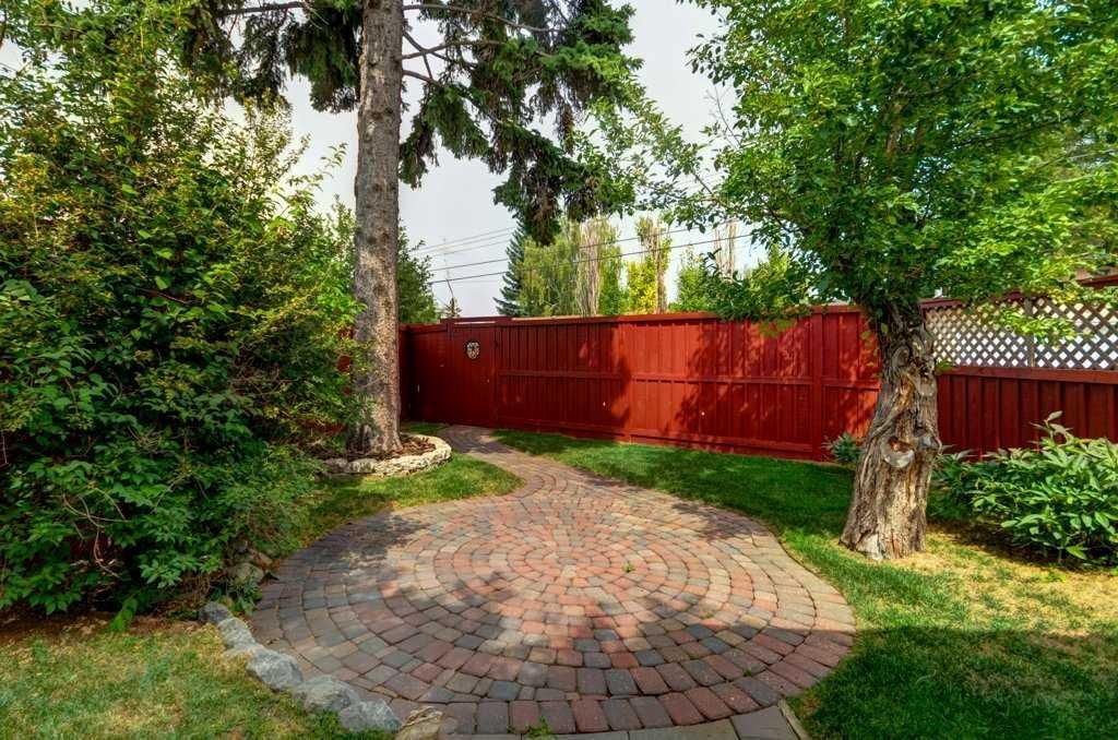 Brick patio in a green backyard with trees and a red wooden fence