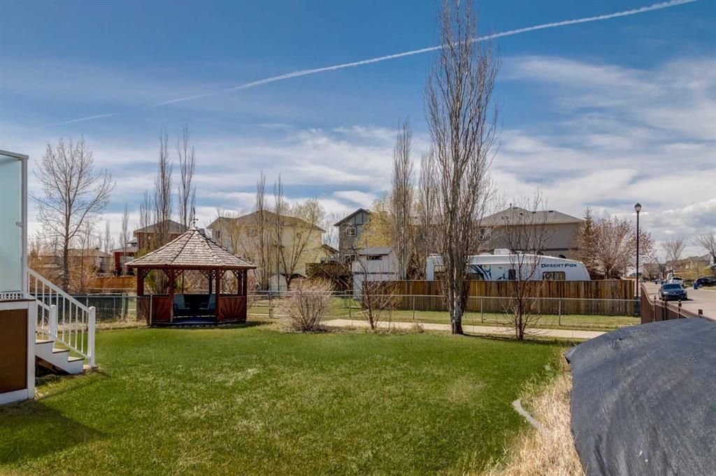 Suburban backyard with green lawn, gazebo, bare trees, houses, and a clear blue sky