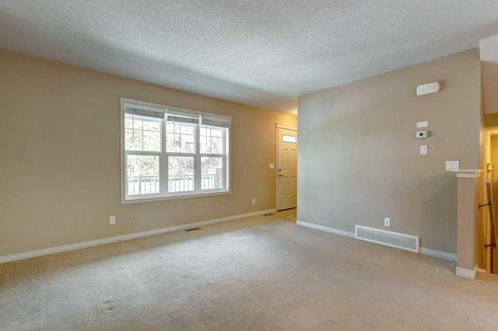 Empty beige living room with carpet, large window, and doorway
