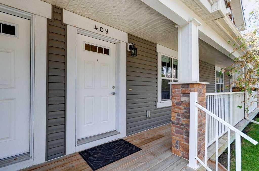 Front porch with white front door, gray siding, brick column, and white railing on a sunny day