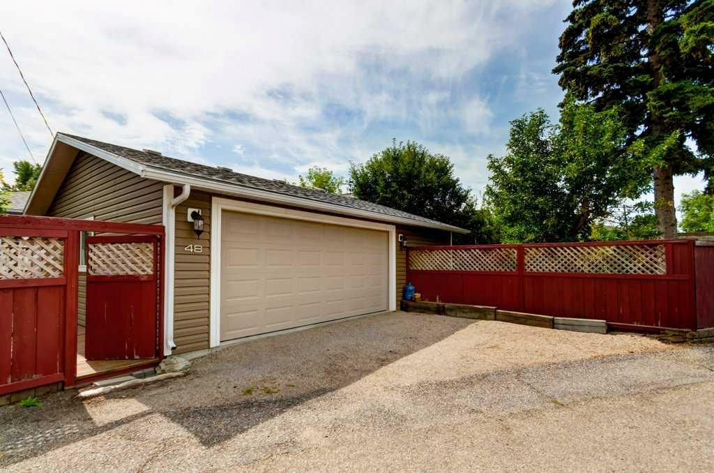 Single-car garage with beige door, red wooden fence, and gravel driveway under a partly cloudy sky