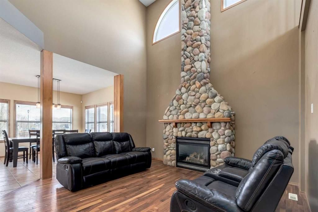 Spacious living room with black leather sofas, wood floors, and a stone fireplace beneath tall windows