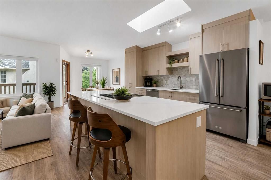 Bright modern kitchen with island, stools, stainless fridge, and open living area with sofa and windows