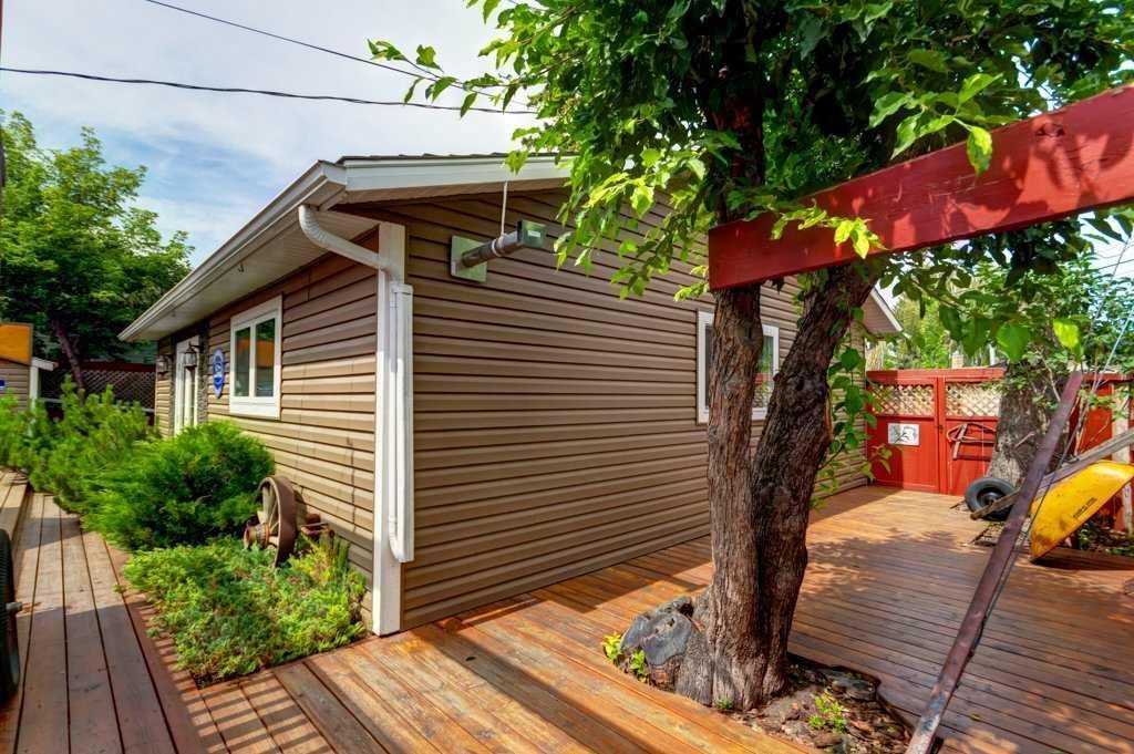 Small brick building beside a wooden deck, with a tree, garden path, and red fence in a sunny yard