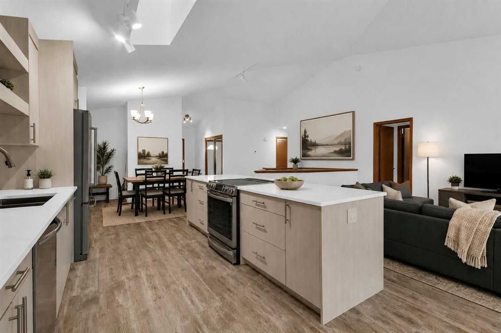 Modern open-concept kitchen and dining area with white cabinets, wood flooring, and a dark sofa in the background
