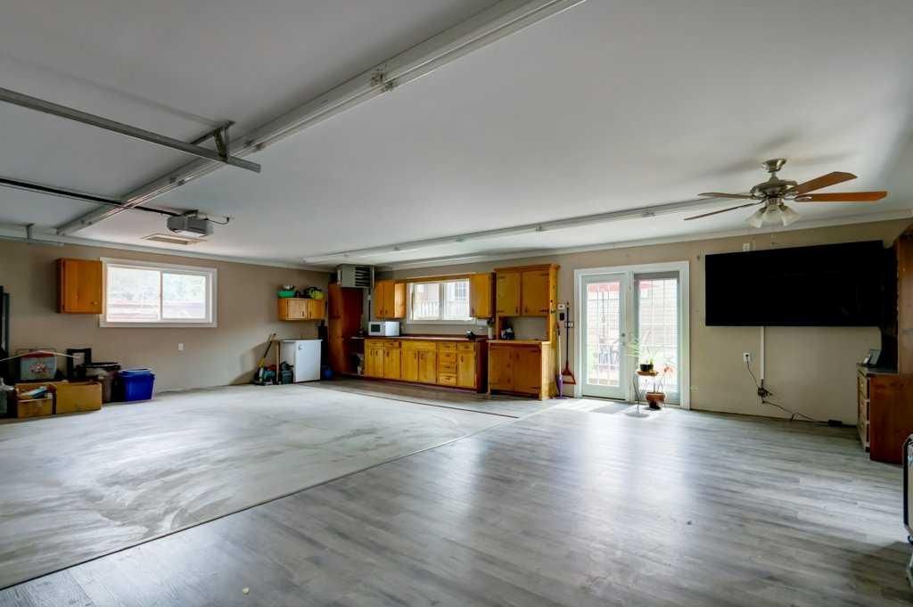 Spacious empty garage with white floor, wood cabinets, windows, and a wall-mounted TV.