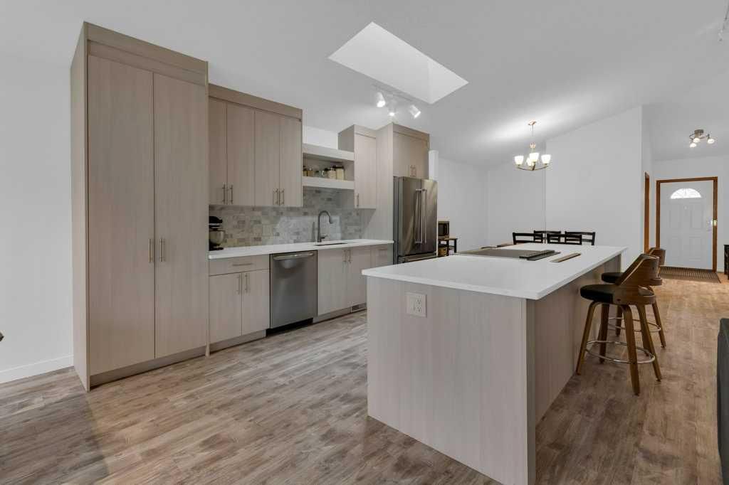 Modern white kitchen with island, wood floors, pendant lights, and dining chairs in a bright open room