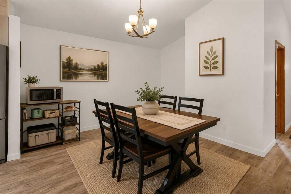 Dining room with wooden table, black chairs, chandelier, side table, and framed wall art on white walls.