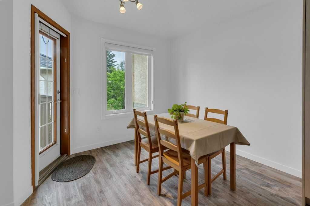 Dining room with wooden table and chairs, white walls, and a glass door letting in daylight.