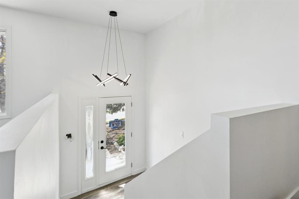 Bright white entryway with staircase, front door, and hanging chandelier.