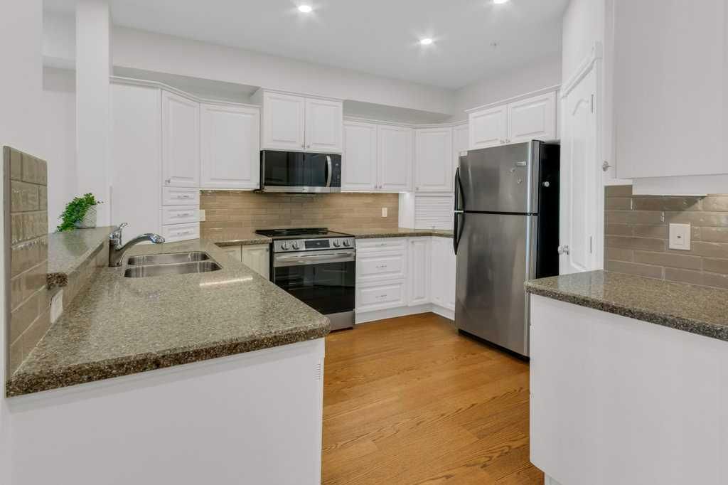 Bright modern kitchen with white cabinets, granite counters, stainless-steel appliances, and wood floors