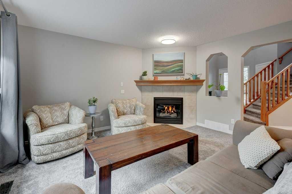 Bright living room with fireplace, beige sofas, wooden coffee table, and staircase to the right.